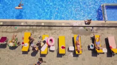 Aerial view from flying drone of people having fun, playing and resting in water in pool. kurt or villa with vacationers. Party of friends or celebration. Sun beds and young people sunbathe in sun.