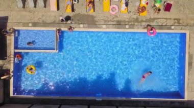 Aerial view from flying drone of people having fun, playing and resting in water in pool. kurt or villa with vacationers. Party of friends or celebration. Sun beds and young people sunbathe in sun.