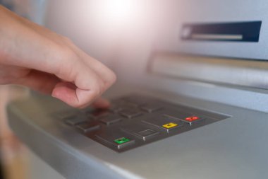 Woman's hand is typing a PIN code on the keyboard of a modern ATM in a shopping center. Selective focus