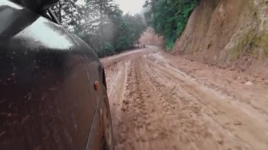 Car moves along road washed out by rains, camera shoots wheel of car inside from cabin. Dirt flies directly into camera lens. impassable places.