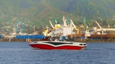 BATUMI, GEORGIA - MAY 22, 2022: Tourist and pleasure boats and yachts ride on sea against backdrop of port and mountains. Touristic place in resort. Rest on water.