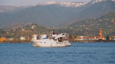 BATUMI, GEORGIA - MAY 22, 2022: Tourist and pleasure boats and yachts ride on sea against backdrop of port and mountains. Touristic place in resort. Rest on water.