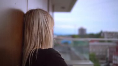 Young and beautiful woman with cup of hot coffee sits on balcony or terrace and looks into distance. holds cup of coffee ore tea in morning. She's in hotel room looking out over nature. Chill out.