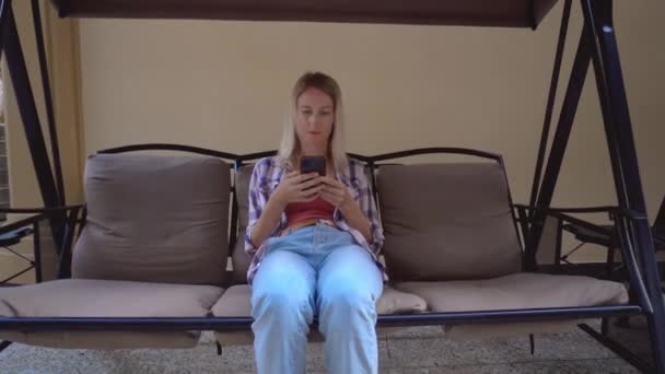 Young Beautiful Blonde Woman Swings Garden Swing Yard Looks Smartphone — Stock video