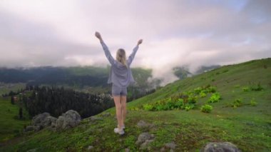 Young girl raised her hands up against background of clouds in high-altitude village in Georgian region of Bakhmaro. She is happy, beautiful view of sky and clouds. Delight overwhelms