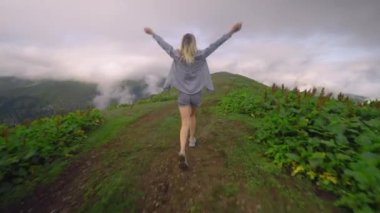 Young girl walks along mountain against background of clouds to high-mountain village in Georgian region of Bakhmaro. She is happy and smiling, beautiful view of sky and clouds. Delight overwhelms
