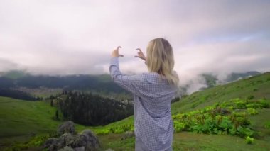 Young girl shows her heart with her fingers against background of clouds in high-altitude village in Georgian district of Bakhmaro. happy, beautiful view of clouds. love for mountains and nature.