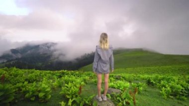 Young girl raised her hands up against background of clouds in high-altitude village in Georgian region of Bakhmaro. She is happy, beautiful view of sky and clouds. Delight overwhelms