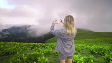 Young girl shows her heart with her fingers against background of clouds in high-altitude village in Georgian district of Bakhmaro. happy, beautiful view of clouds. love for mountains and nature.