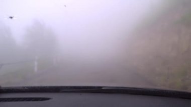 First-person view of driver of car driving down road with thick fog or smog. View from inside car, poor visibility. Countryside, road through forest and mountains.
