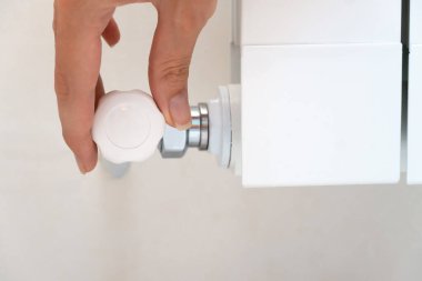 Close-up of a woman's hand twisting the temperature controller of a water heating system in a modern house, a light background. New steel radiator for residential premises