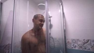 Man taking shower, person shower cabin in home lifestyle. Morning body care for young people. guy fools around and draws his heart with his finger on condensed glass. Valentine's Day.