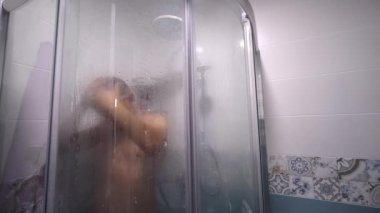 Man taking shower washes his hair underwater in shower in shower. Person's shower in home lifestyle. Morning body care routine for young adults. guy sings and fools around to music.