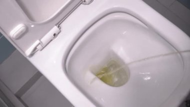 Person stands in modern toilet, and pees in first person. stream of urine flies directly into opening of toilet. Then he pours everything with clean water. Modern renovation of toilet room.