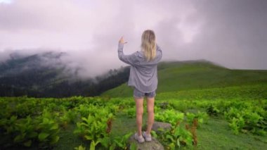 Young girl shows her heart with her fingers against background of clouds in high-altitude village in Georgian district of Bakhmaro. happy, beautiful view of clouds. love for mountains and nature.