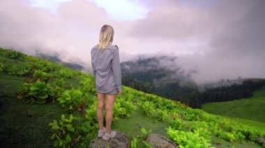 Young girl raised her hands up against background of clouds in high-altitude village in Georgian region of Bakhmaro. She is happy, beautiful view of sky and clouds. Delight overwhelms