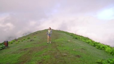 Young girl walks along mountain against background of clouds to high-mountain village in Georgian region of Bakhmaro. She is happy and smiling, beautiful view of sky and clouds. Delight overwhelms