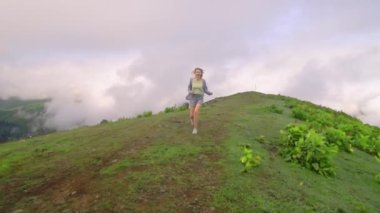 Young girl walks along mountain against background of clouds to high-mountain village in Georgian region of Bakhmaro. She is happy and smiling, beautiful view of sky and clouds. Delight overwhelms