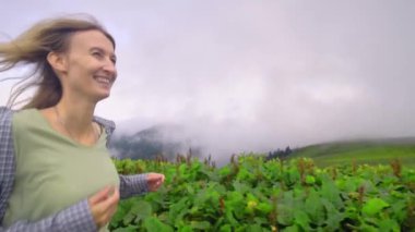 Young girl walks along mountain against background of clouds to high-mountain village in Georgian region of Bakhmaro. She is happy and smiling, beautiful view of sky and clouds. Delight overwhelms