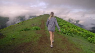 Young girl walks along mountain against background of clouds to high-mountain village in Georgian region of Bakhmaro. She is happy and smiling, beautiful view of sky and clouds. Delight overwhelms