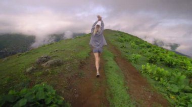 Young girl walks along mountain against background of clouds to high-mountain village in Georgian region of Bakhmaro. She is happy and smiling, beautiful view of sky and clouds. Delight overwhelms