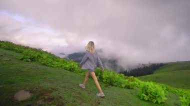 Young girl raised her hands up against background of clouds in high-altitude village in Georgian region of Bakhmaro. She is happy, beautiful view of sky and clouds. Delight overwhelms