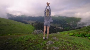 Young girl raised her hands up against background of clouds in high-altitude village in Georgian region of Bakhmaro. She is happy, beautiful view of sky and clouds. Delight overwhelms