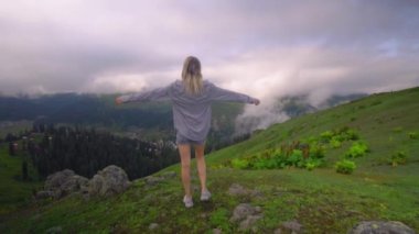Young girl raised her hands up against background of clouds in high-altitude village in Georgian region of Bakhmaro. She is happy, beautiful view of sky and clouds. Delight overwhelms