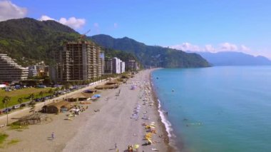 Aerial view on beach and umbrellas. Beach and blue water of sea against background of city and mountains. Top view from drone to beach. View of beach with colorful umbrellas, bathing people