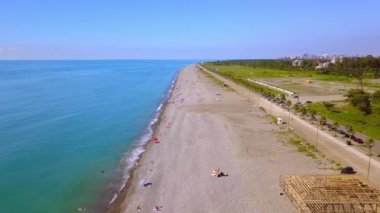 Aerial view on beach and umbrellas. Beach and blue water against backdrop of big city. Top view from drone at beach and azure sea. View of beach with colorful umbrellas, bathing people in water