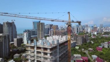 Construction of new multi-storey buildings. Construction crane on construction site against backdrop of mountains sea city. View from drone. New apartments and real estate development. Batumi, Georgia