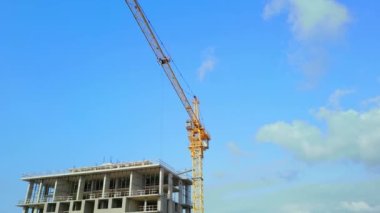 Drone flight of construction crane on construction site with constructed building. Against background of blue sky and clouds. Housing construction, apartment block. Real estate and developer. Business