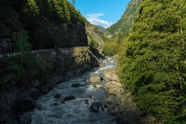 Stormy mountain river flows along the serpentine road among the mountains on a sunny autumn day. Beautiful, atmospheric autumn landscape with a mountain river