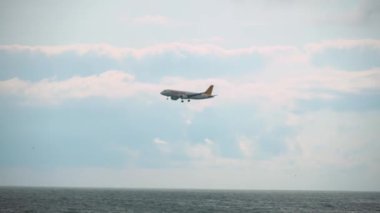 BATUMI, GEORGIA - June 22, 2022: Commercial passenger plane or cargo transport fly over coast of sea landing at airport, hiding behind houses of city.