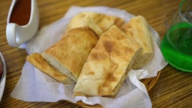 Dilimlenmiş beyaz ekmek, Pita ekmeği ya da yassı ekmek şeklinde restoranda masanın üzerinde. Yatak peçetesi, Gürcistan kafesinde bulaşık servisi. Yeşil limonata ve sosun yanında. Kamera döndürmesi.