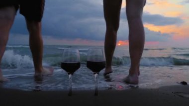 Young woman man enters ocean or sea knee-deep against backdrop of beautiful sunset and glasses of red wine of rare plan. Honeymoon or romantic relationships of lovers. Love. Valentine's day.