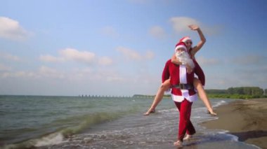 Noel tatili. Noel Baba şapkalı seksi kadın sıcak bir günde sahilde Noel Baba 'ya biniyor. Onlar mutlu. Komik ve mutlu. Sıcak hava, sıcak ve egzotik iklim. Burada kal. Yeni Yıl.