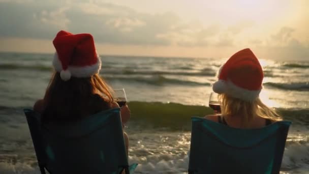 Ευτυχισμένα Κορίτσια Μπικίνι Κάθονται Καρέκλες Γιορτάζοντας Χριστούγεννα Στην Παραλία Πίνοντας — Αρχείο Βίντεο