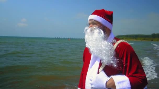 Takım Elbiseli Noel Baba Deniz Kıyısında Omzunda Torbayla Yürüyor Sahilde — Stok video