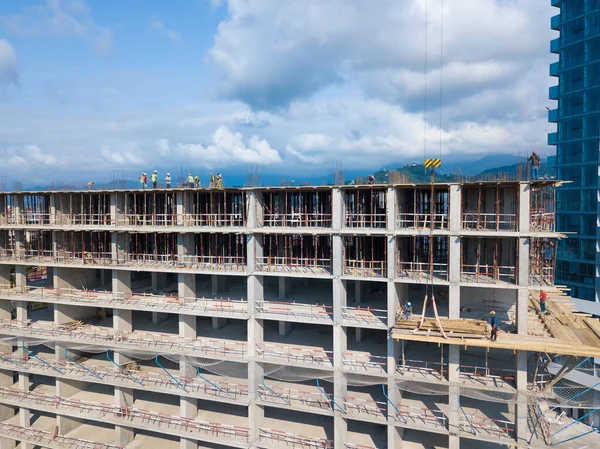 Drone view of the construction site, builders on the top floor of a building under construction against the backdrop of mountains on a sunny day