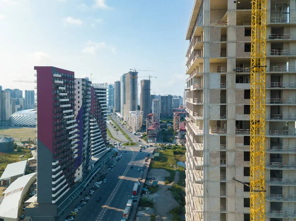 Drone view of an almost completed residential multi-storey building with a tower crane overlooking the city street on a sunny day. Multi-storey residential building is being built using a crane.