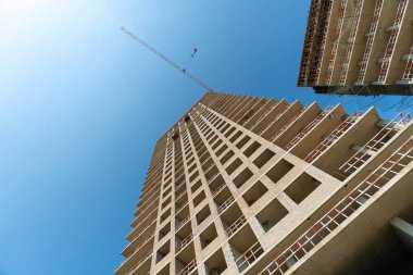 Multi-storey building under construction with a construction crane against the sky on a sunny day. Bottom view