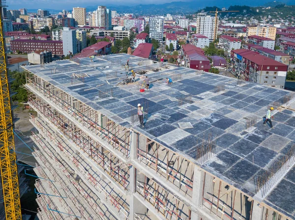 Drone view of the construction site, builders on the top floor of a building under construction against the backdrop of mountains on a sunny day top view