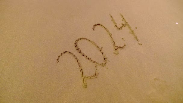 図2024ビーチの黄金の砂の上に 大晦日のコンセプト 泡の波と海岸線の砂の上に描かれた部屋のトップビュー 水の波の碑文を洗い流す クリスマスと新年のコンセプト — ストック動画