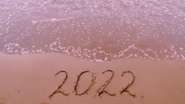 図2022ビーチの黄金の砂の上に 大晦日のコンセプト 泡の波と海岸線の砂の上に描かれた部屋のトップビュー 水の波の碑文を洗い流す クリスマスと新年のコンセプト — ストック動画