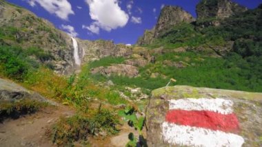 Georgia Shdugra 'da güzel bir şelale. Turist Cazibesi. Dağda pembe çiçekler yetişir, şelale nehre akar. Taştaki damga turistleri yönlendirmek için boyanmış..