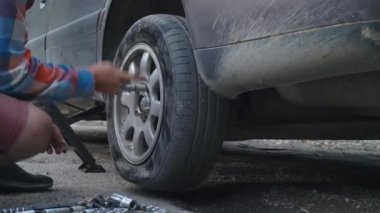 Tekerleği patlamış lastiği değiştirmek için arabanın tekerleğini sökmüş. Yol, yolculuk tekerleği kırılır. Aletlerin arka planında patlak lastiğin değiştirilmesi. Yardım.