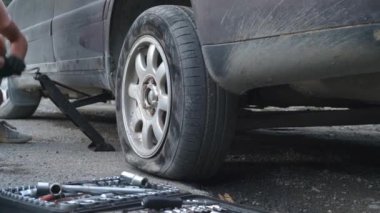 Adam patlamış lastiği değiştirmek için arabayı Doncrat 'a kaldırıyor. Yol, yolculuk tekerleği kırılır. Aletlerin arka planında patlak lastiğin değiştirilmesi. yardım.