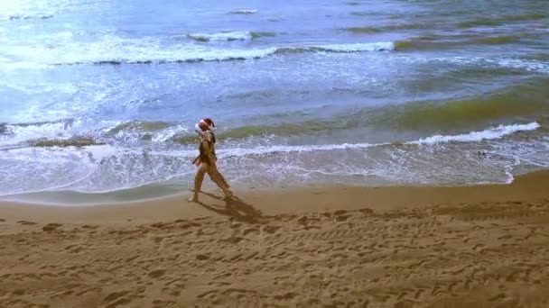 クリスマスビーチ休暇サンタの帽子とビキニで女性を旅行熱帯のビーチで冬の休憩をお楽しみください 女の子は海を歩いて景色を楽しむ 空中写真又はドローン写真 — ストック動画