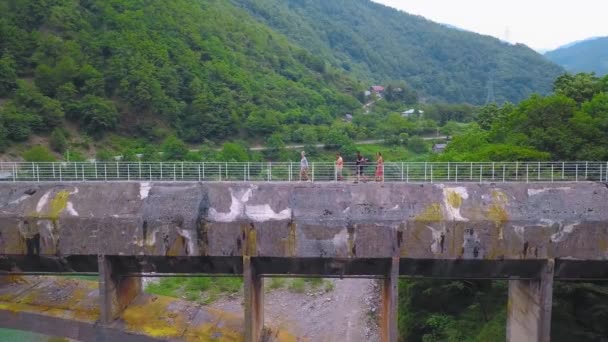 4人で構成される会社は ジョージア州の山や川を背景に峡谷を渡る大きなコンクリートの歩道橋を渡っています 観光客は地域を探索し 古代の橋のドローンの形でランドマーク — ストック動画